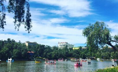 Scenic view of Burnham Park's boating lake in Baguio City, Philippines, with colorful paddle boats and lush greenery.
